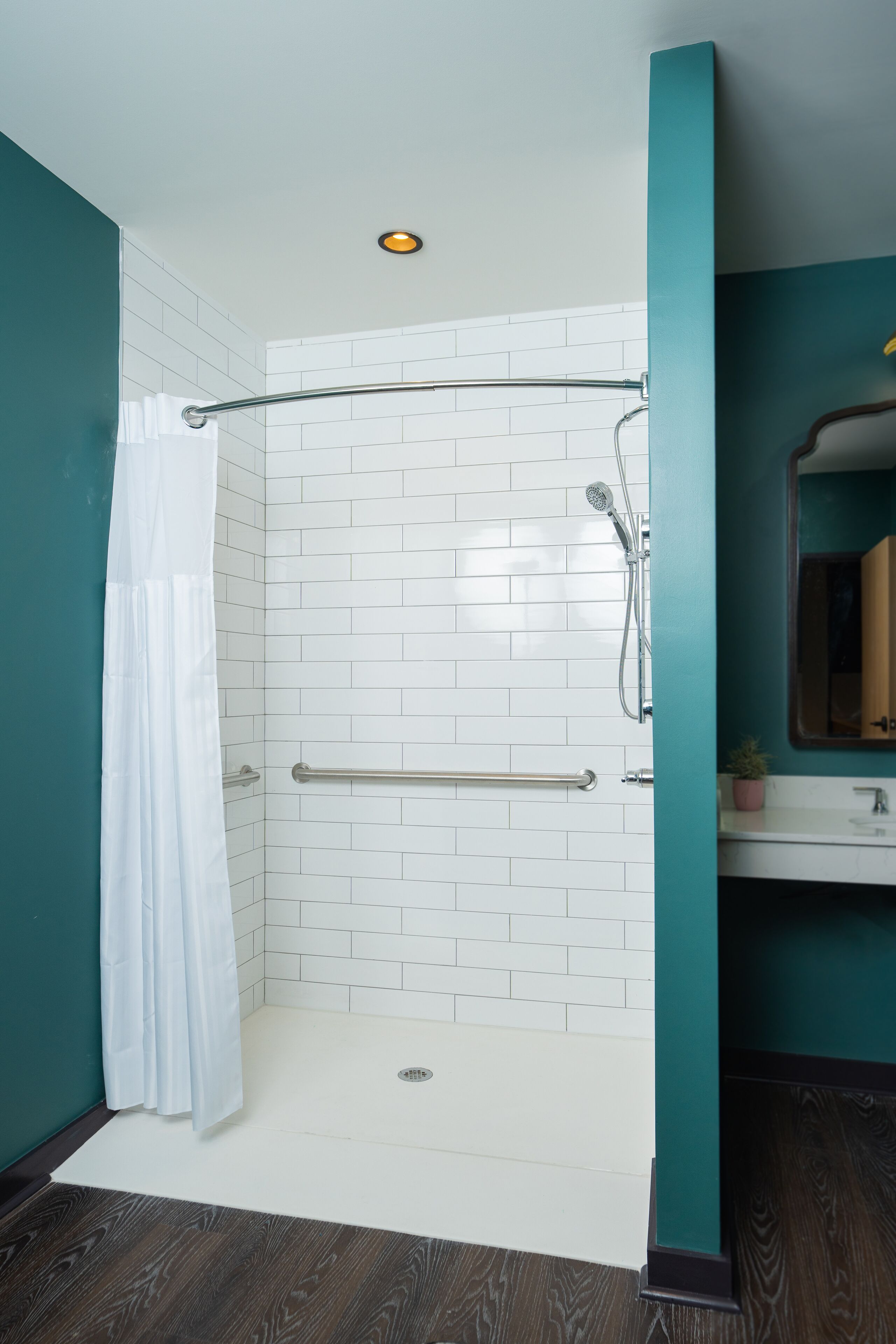 Un baño moderno con paredes de azulejos blancos, una ducha con puerta de vidrio y suelo de madera.