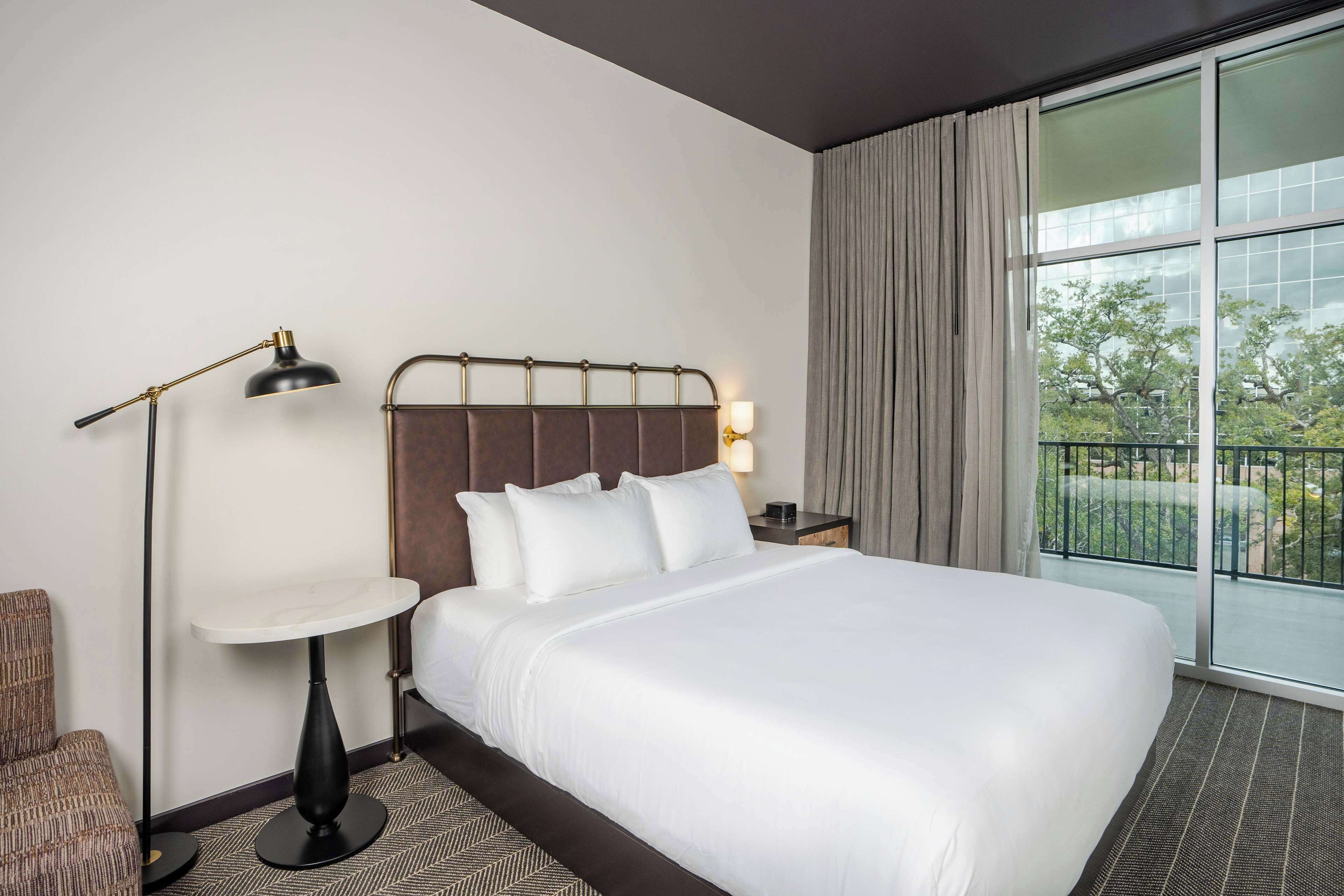 Une chambre d’hôtel avec un grand lit, une table de chevet, une lampe et une vue sur l’extérieur.