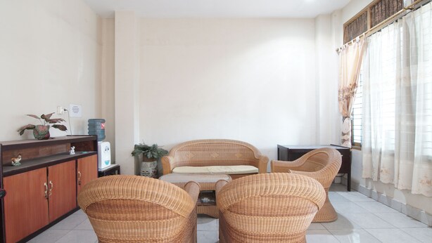 Una sala de estar con muebles de mimbre, un sofá y una mesita de centro. Se observa un mueble con una planta encima.
