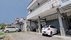 Un edificio de dos pisos con área de estacionamiento techada, un coche blanco estacionado al frente y una motocicleta adentro.