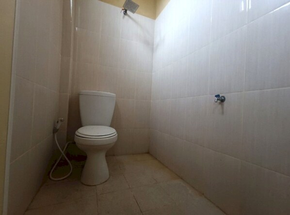 A small, white-tiled bathroom with a toilet, a shower, and a wall-mounted faucet.