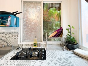 Une cuisine équipée d’une cuisinière à gaz, d’un évier, d’une fenêtre donnant sur un espace verdoyant et d’une plante en pot.