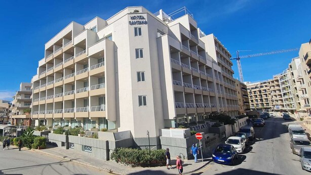 A multi-story hotel with balconies, a visible sign for a grocery store, and a clear blue sky. - COMFORTABLE THREE BEDROOM APARTMENT WITH WIFI & LOCATED IN THE CENTRE  (QAWRA)