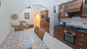 A compact kitchen with wooden cabinets, a dining table with a colorful tablecloth, and a small seating area with wicker chairs. - COMFORTABLE THREE BEDROOM APARTMENT WITH WIFI & LOCATED IN THE CENTRE  (QAWRA)