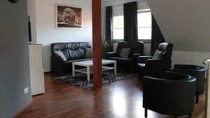 A modern living room with a sofa, chairs, a coffee table, and a large window with curtains. - Schöne Eigentumswohnung mit Terrasse für 2 Pers (Bippen)