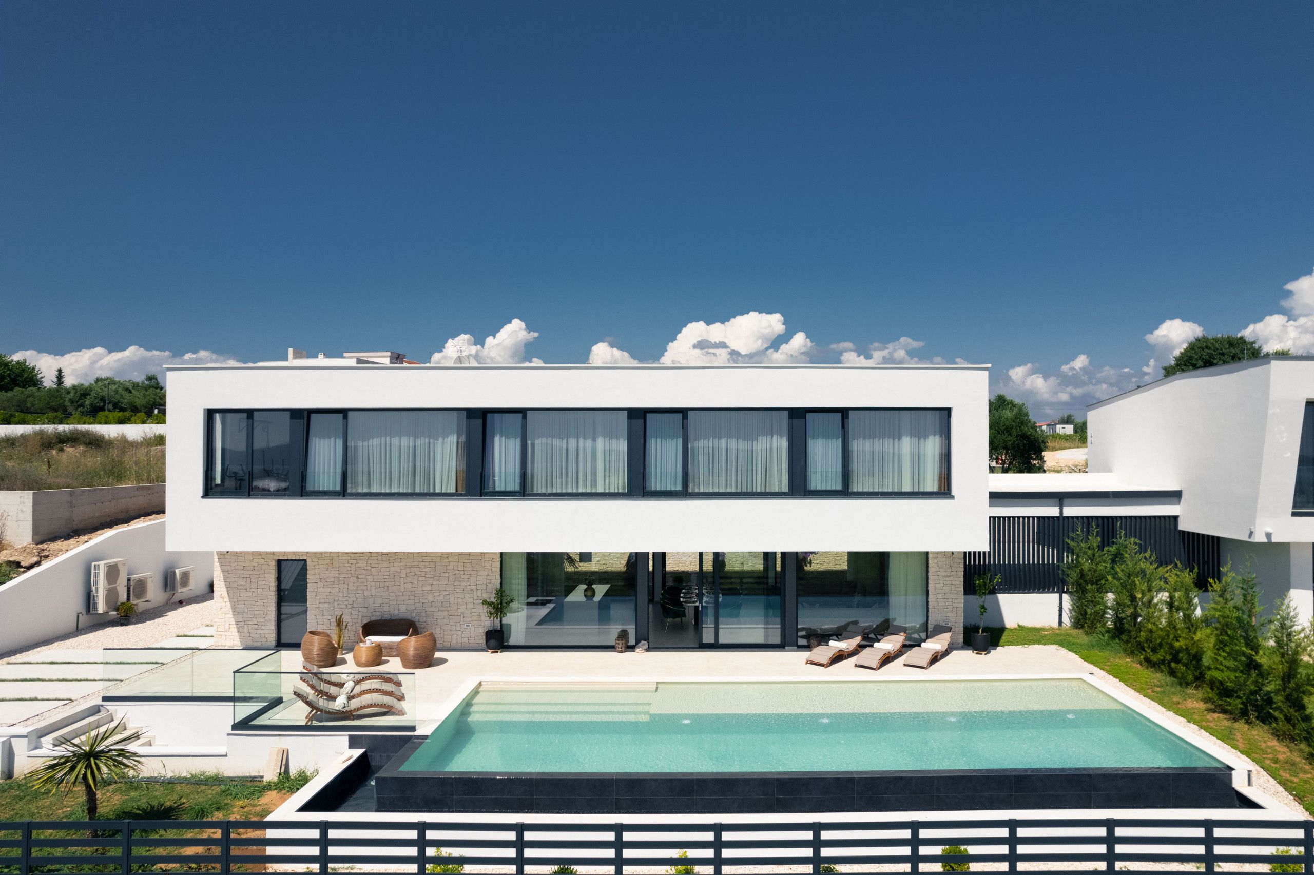 A modern two-story house with a swimming pool, outdoor seating, and a clear view of the sky.
