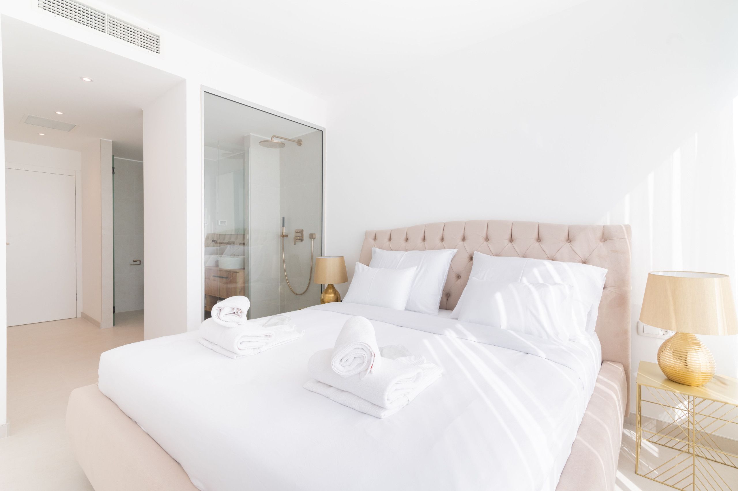 Una habitación de hotel moderna con una cama grande, cabina de ducha de vidrio y una mesita de noche con lámpara.