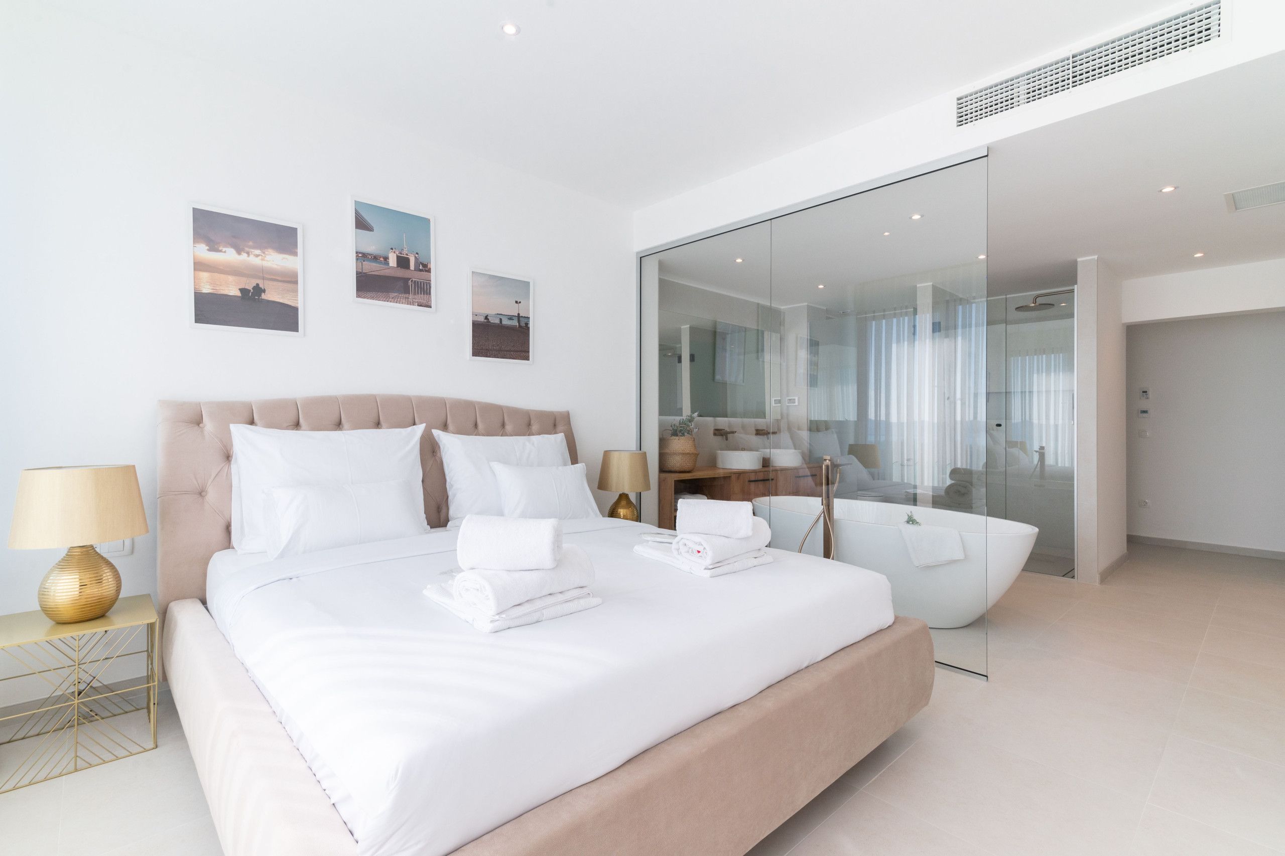 A modern hotel room with a large bed, a glass shower enclosure, and a view of the sea.