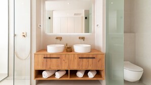 Une salle de bain moderne avec deux lavabos, un grand miroir et une douche à l’italienne.