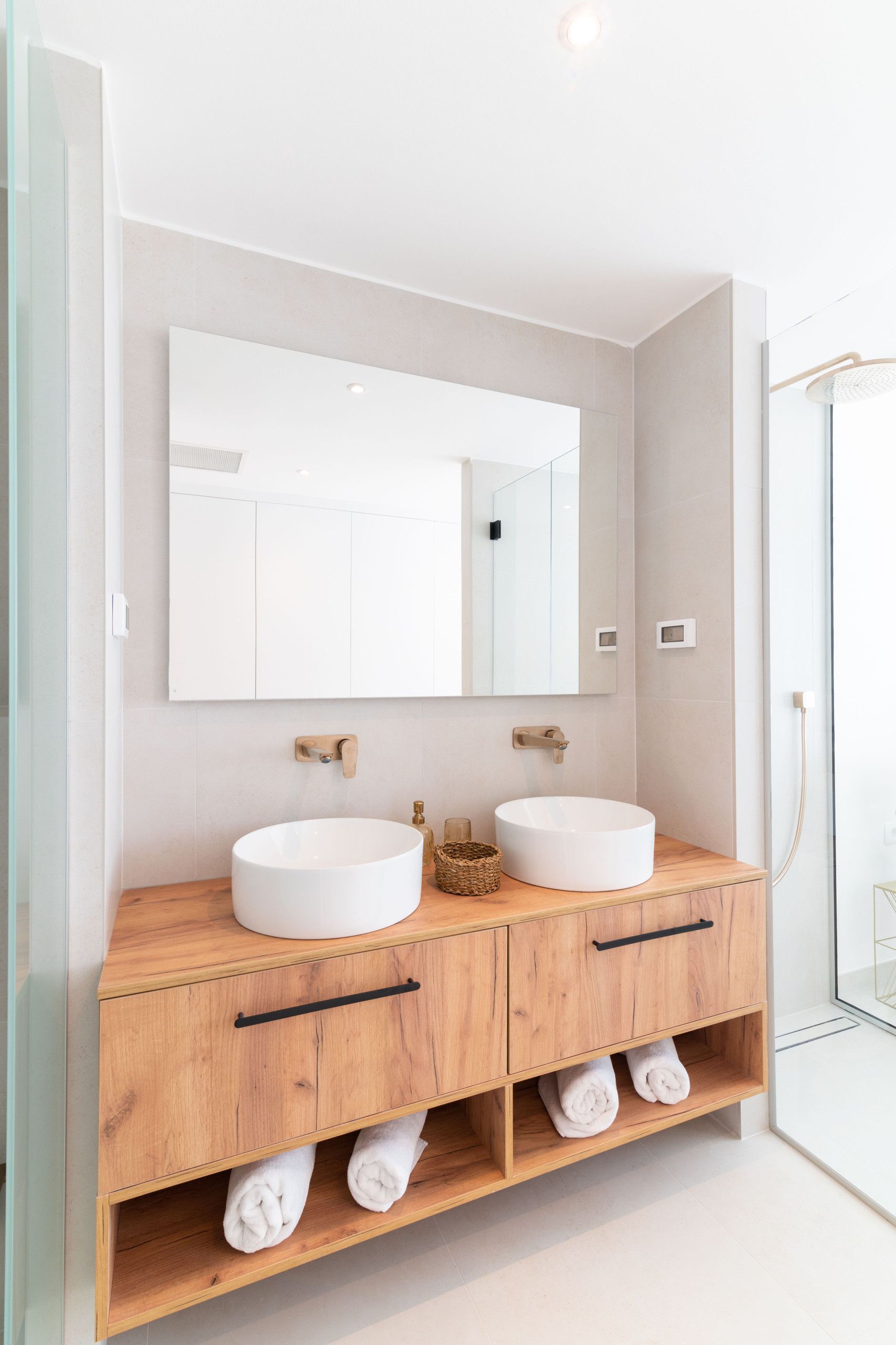 A modern bathroom with two sinks, a large mirror, and wooden cabinetry.