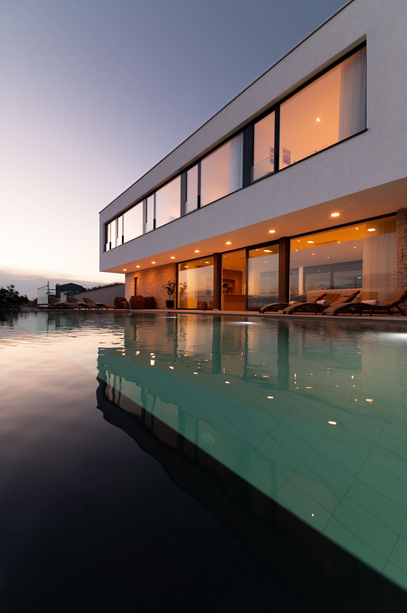Une maison moderne dotée d’une piscine, de grandes fenêtres et d’un espace salon extérieur.