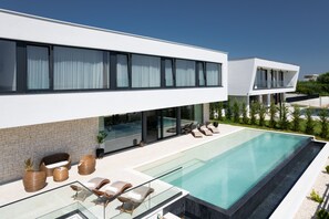 Ein modernes Haus mit Swimmingpool, Sitzgelegenheiten im Freien und Blick auf die Umgebung.