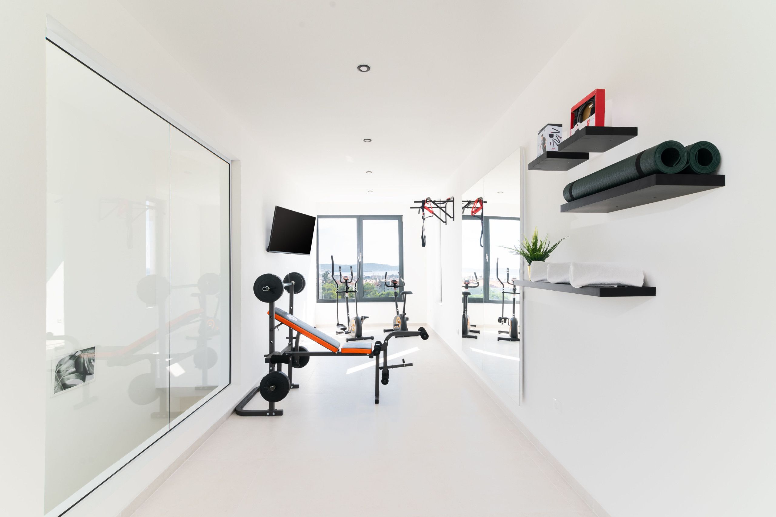 A modern gym with exercise equipment, a TV, and a large window offering a view.