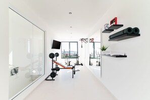 Une salle de sport moderne équipée de matériel d’exercice, d’un téléviseur et d’une grande fenêtre donnant sur un paysage agréable.