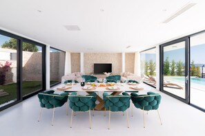 A modern dining area with a large table, teal chairs, and a TV on the wall.