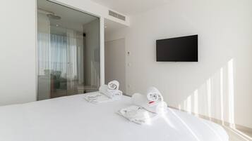 A modern hotel room with a large bed, a flat-screen TV mounted on the wall, and a glass door leading to a bathroom.