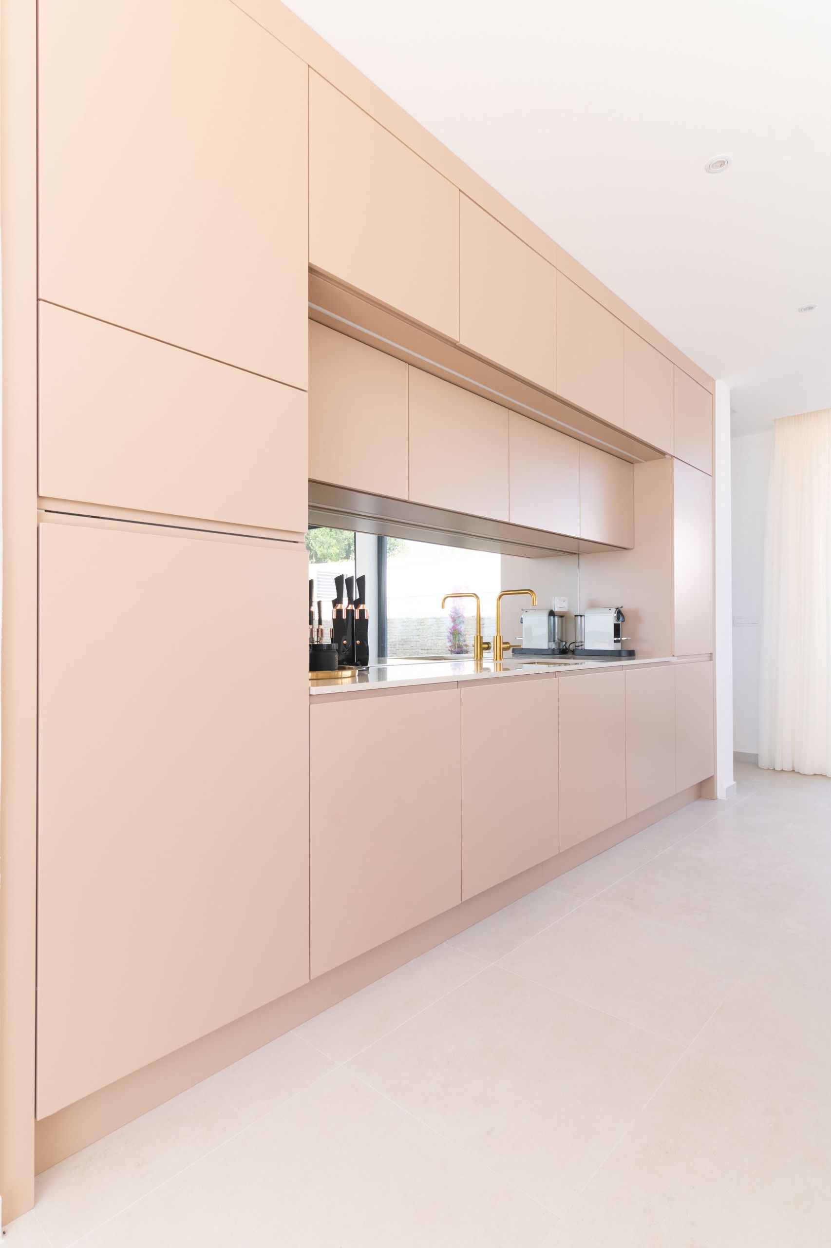 A modern kitchen with light-colored cabinets, a stainless steel range hood, and a countertop with a coffee machine and kitchenware.