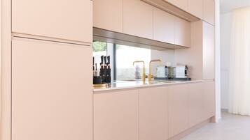 A modern kitchen with light-colored cabinets, a stainless steel range hood, and a countertop with a coffee machine and kitchenware.