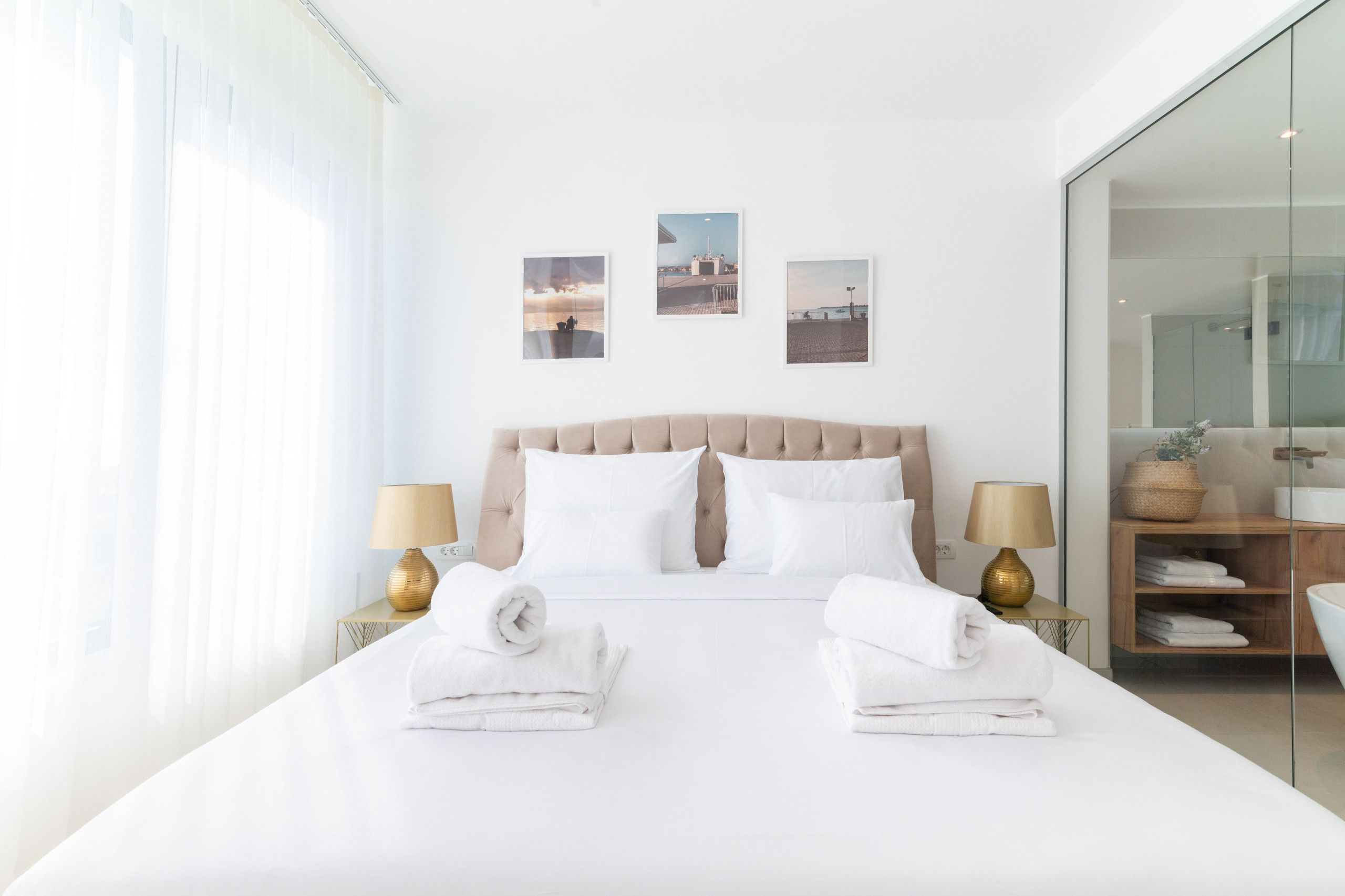 Una habitación de hotel moderna con una cama grande, dos mesitas de noche con lámparas, un box de ducha de vidrio y tres cuadros en la pared.