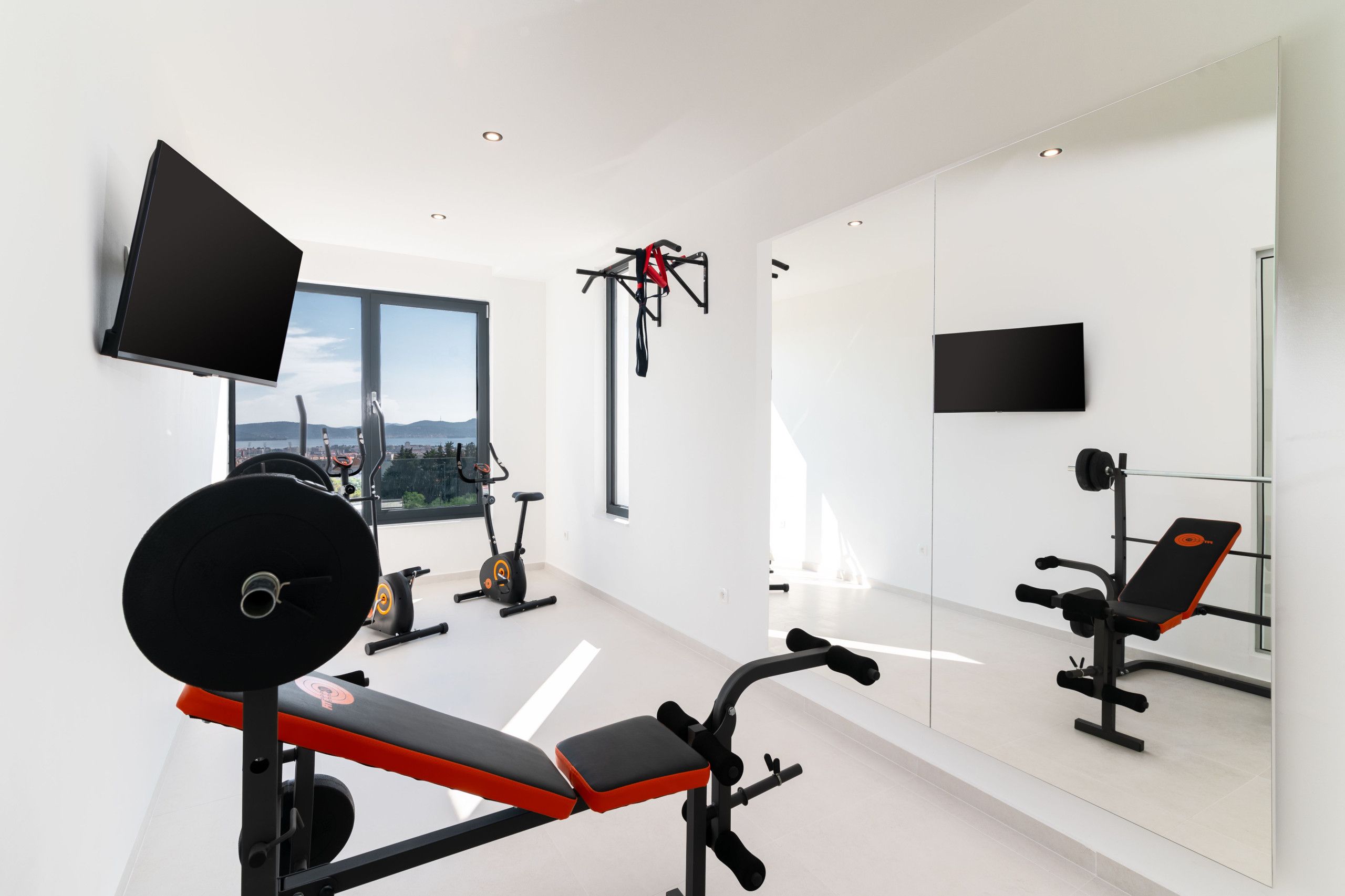A modern gym with a large window, exercise equipment, and a TV mounted on the wall.