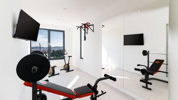 A modern gym with a large window, exercise equipment, and a TV mounted on the wall.