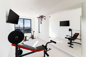 Un gimnasio moderno con un amplio ventanal, equipamiento de ejercicio y una televisión montada en la pared.