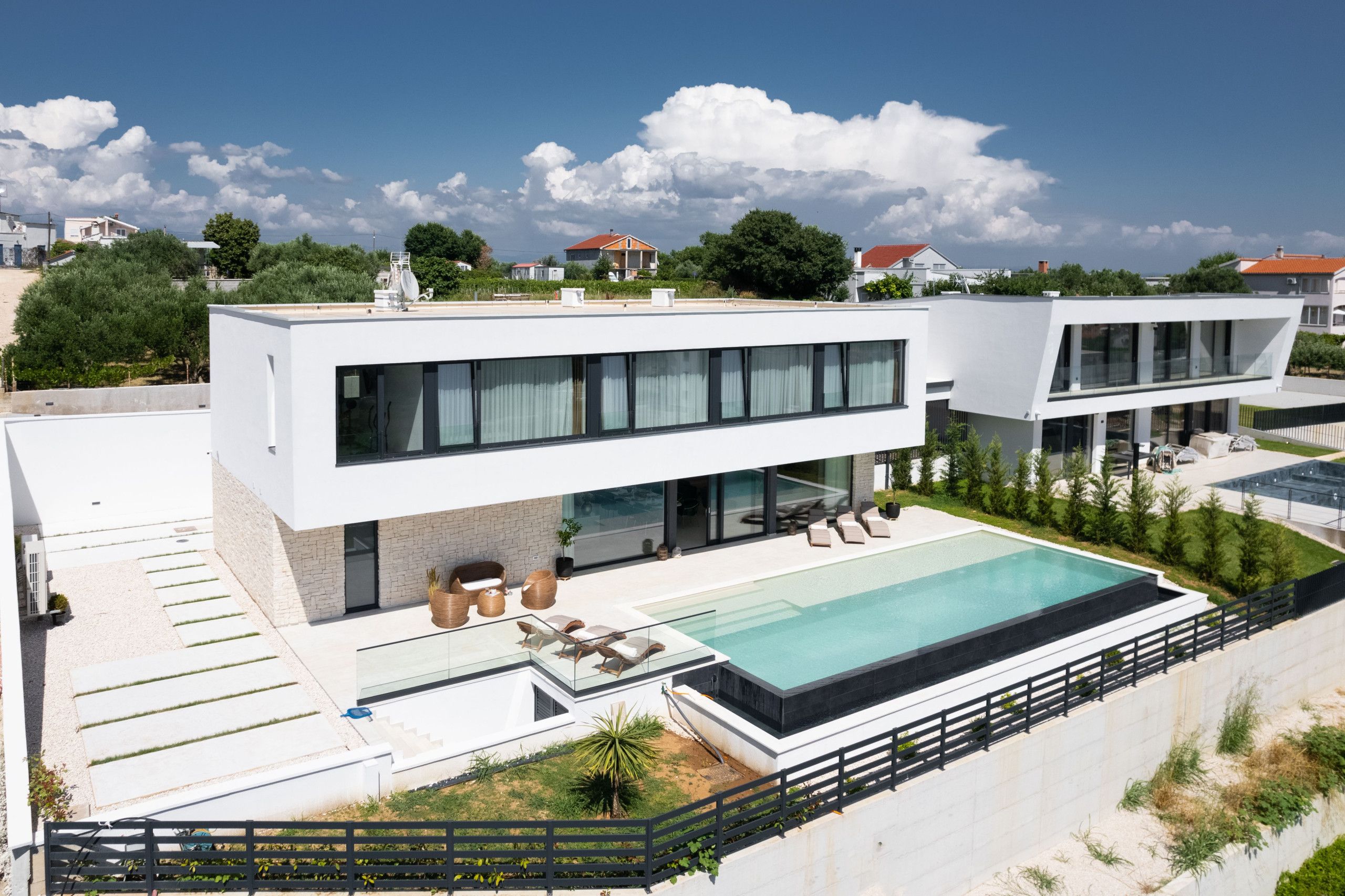 A modern two-story house with a swimming pool, outdoor seating, and a well-maintained garden.