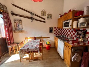 A cozy kitchen with wooden cabinets, a checkered backsplash, and a dining area with a table set for two.