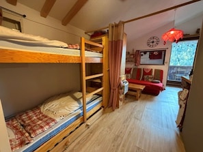 A bunk bed room with a wooden ladder, a small table, and a red sofa.