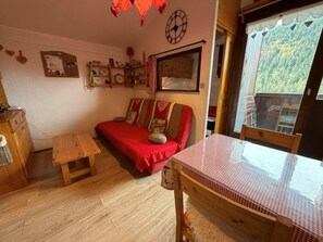 Una sala de estar acogedora con un sofá rojo, una mesa de madera y una ventana con vista a zonas verdes.