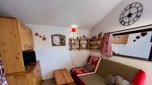 A cozy living room with a wooden cabinet, a small table, a sofa with heart-patterned cushions, and a wall clock.