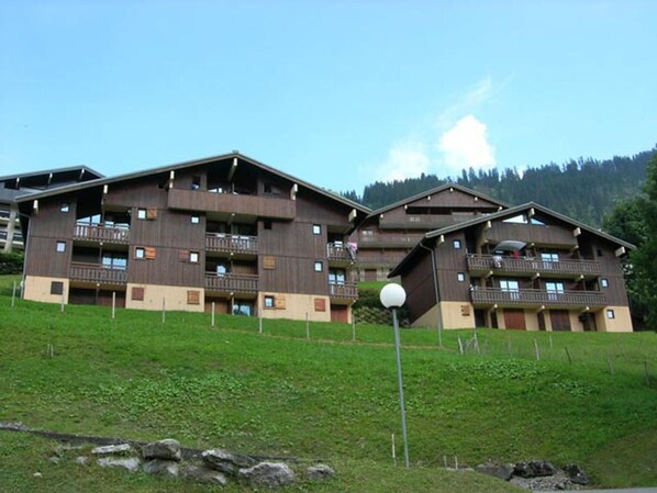 Un edificio de madera de varios pisos con balcones, frente a colinas verdes y un cielo despejado.