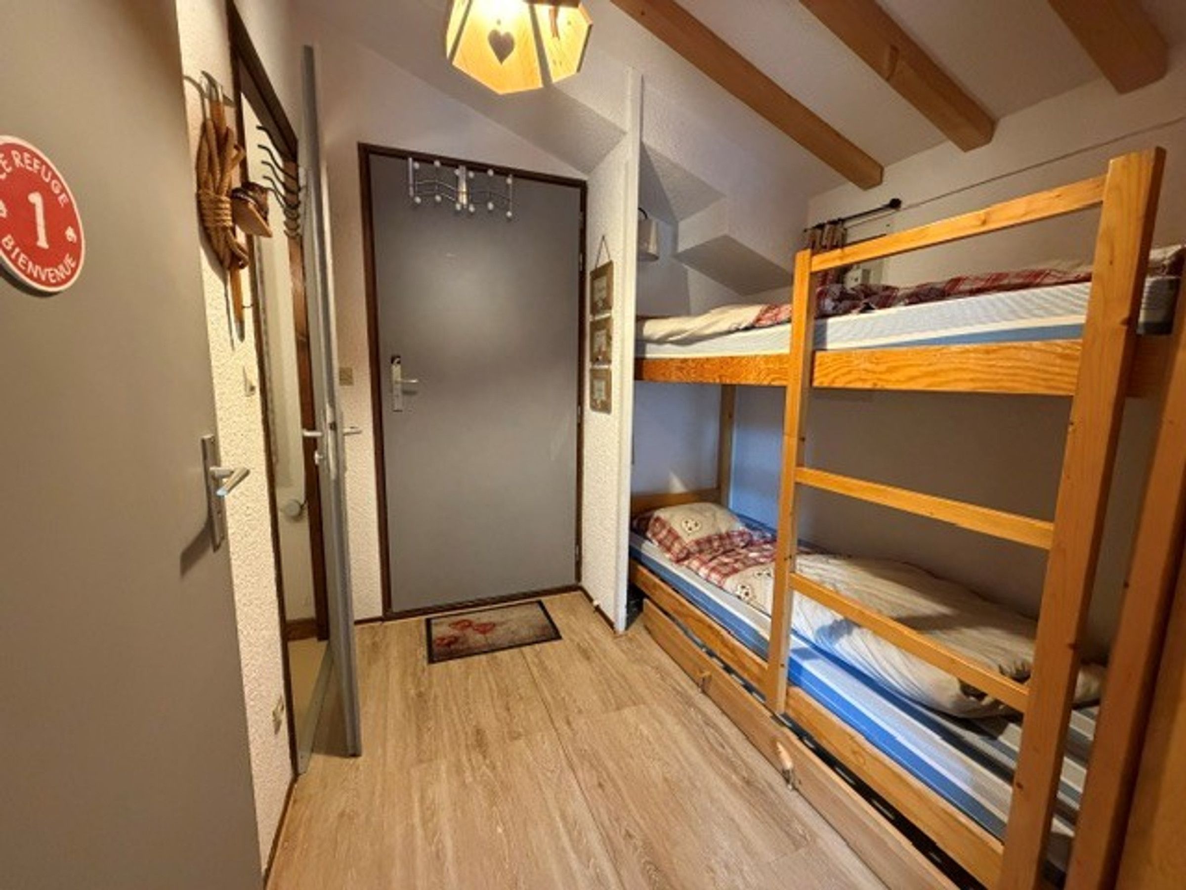 Un couloir étroit avec un lit superposé en bois, une porte avec une pancarte et un plafond en bois.