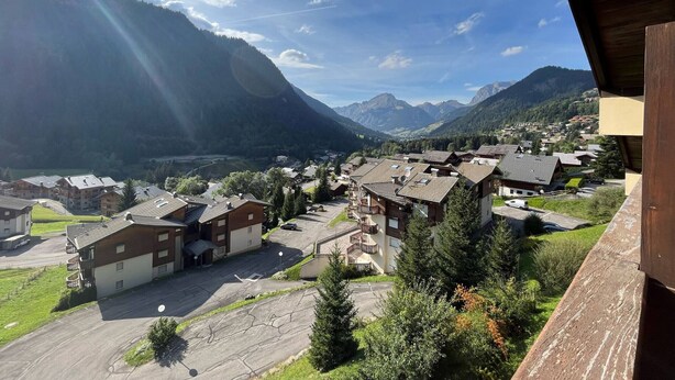 A mountain village with traditional buildings, a paved road, and a valley.