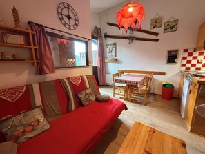 Una sala de estar acogedora con un sofá rojo, una mesa de comedor de madera y una cocina con un salpicadero a cuadros rojo y blanco.