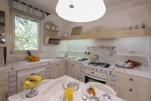 A modern kitchen with a large window, white cabinetry, and a dining area with breakfast items. - Breathtaking views in a quiet part of Taormina, a stone's throw from downtown (Taormina)