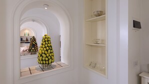 Un couloir avec un mur blanc, une fenêtre ornée d’un panier de citrons et une étagère sur laquelle se trouvent un bol et un verre.
