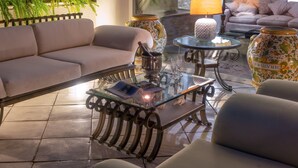 Un salon comprenant un canapé, des fauteuils, une table basse en verre, des vases décoratifs et une lampe.