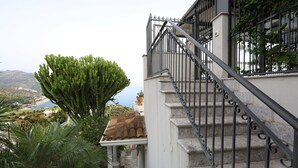 Un escalier orné d’une rampe en fer forgé menant à un balcon d’où l’on peut admirer un paysage côtier.