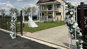 A two-story house with a balcony, surrounded by a fence and decorated with white floral arrangements. - Pensiunea Ramina (Adjud)