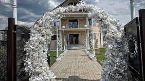 A two-story building with a central entrance, flanked by white floral decorations. - Pensiunea Ramina (Adjud)