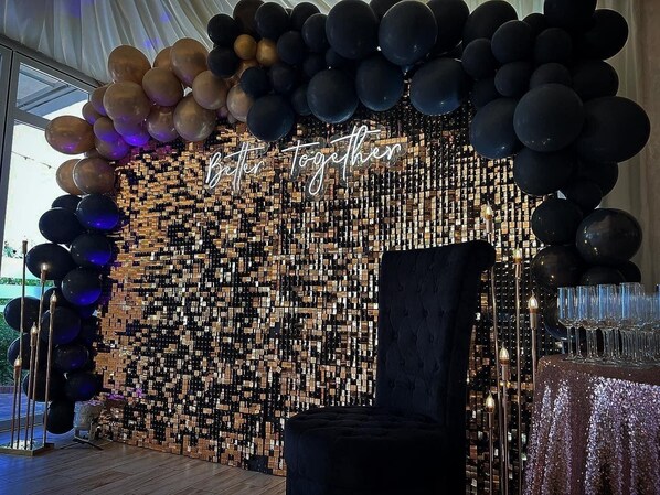 A room with a black and gold balloon arch, a mirrored wall, and a table with glasses.