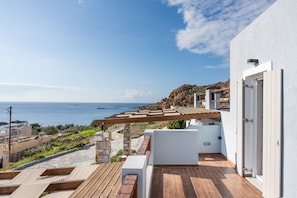 Eine Dachterrasse mit Meerblick, Steinpfeilern, einer Holzpergola und einem weißen Gebäude.