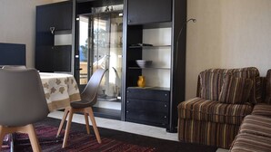 A modern living room with a dining area, featuring a sofa, a dining table with a chair, and a black cabinet with glass doors.