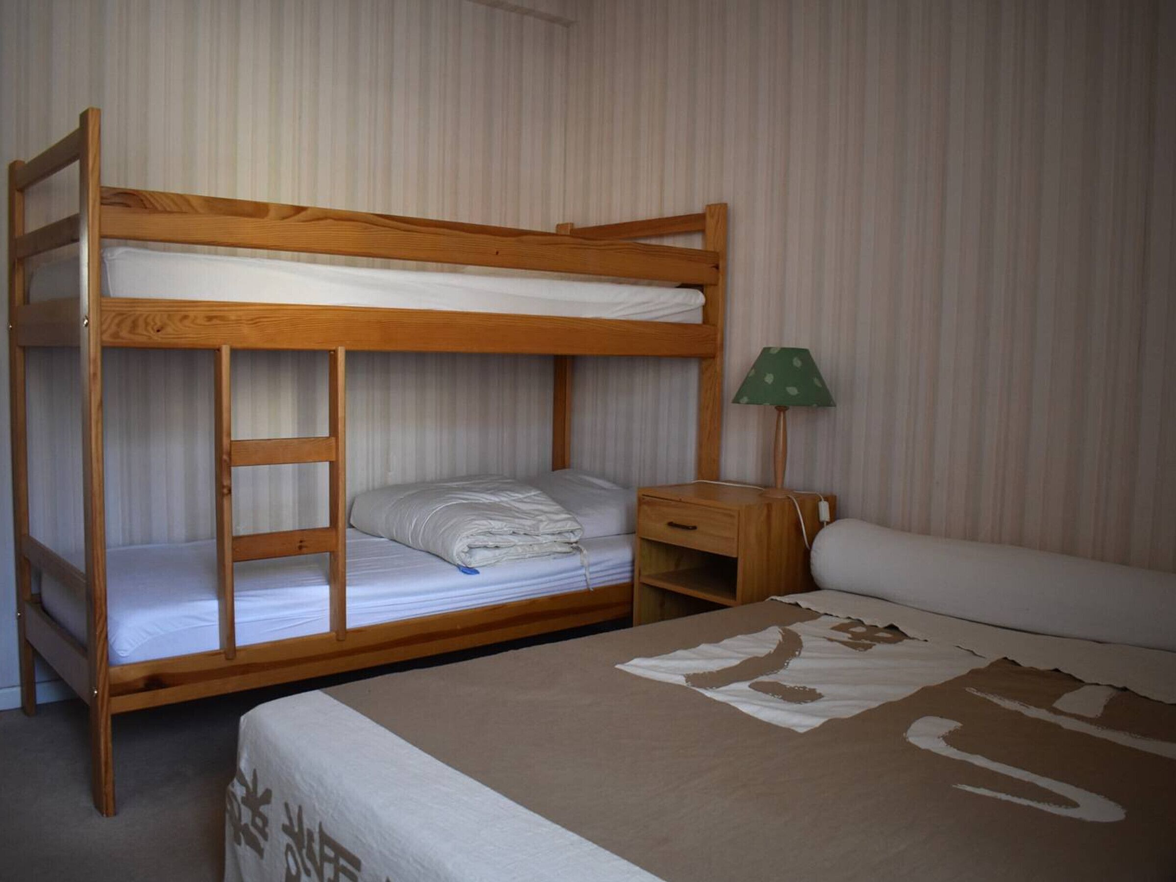 Habitación con literas de madera, una mesita de noche con lámpara y una cama con colcha estampada.