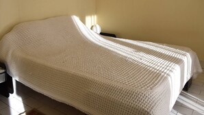 A single bed with a white blanket in a room with a plain yellow wall and a small framed picture.