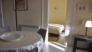 A hotel room with a round dining table, a bed with a white bedspread, a small bedside table with a lamp, and a picture on the wall.