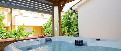 Uma banheira de hidromassagem sob uma pérgola de madeira, com vista para uma área residencial.