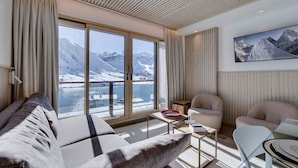 A modern living room with a large window offering a view of a snowy mountain and lake. There is a sofa, a chair, and a small table with a bowl and a book. - Charming renovated apartment for 4 in Tignes with lake view (Tignes)