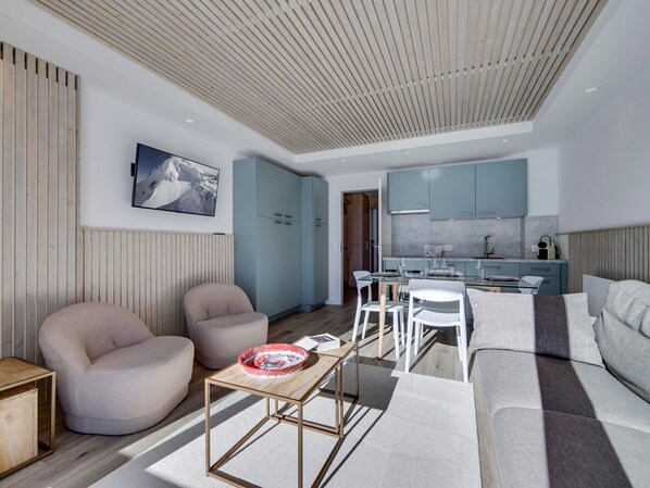A modern living room with a wooden ceiling, a dining area with a table and chairs, and a kitchen with light blue cabinets. - Charming renovated apartment for 4 in Tignes with lake view (Tignes)
